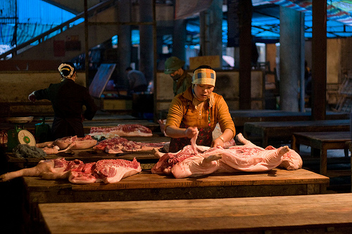 At the Sunday market in Sapa, northern Vietnam, women butcher hogs slaughtered outside of town but still steaming when they start working on them at the market (image via Flickr/Kurt Johnson).